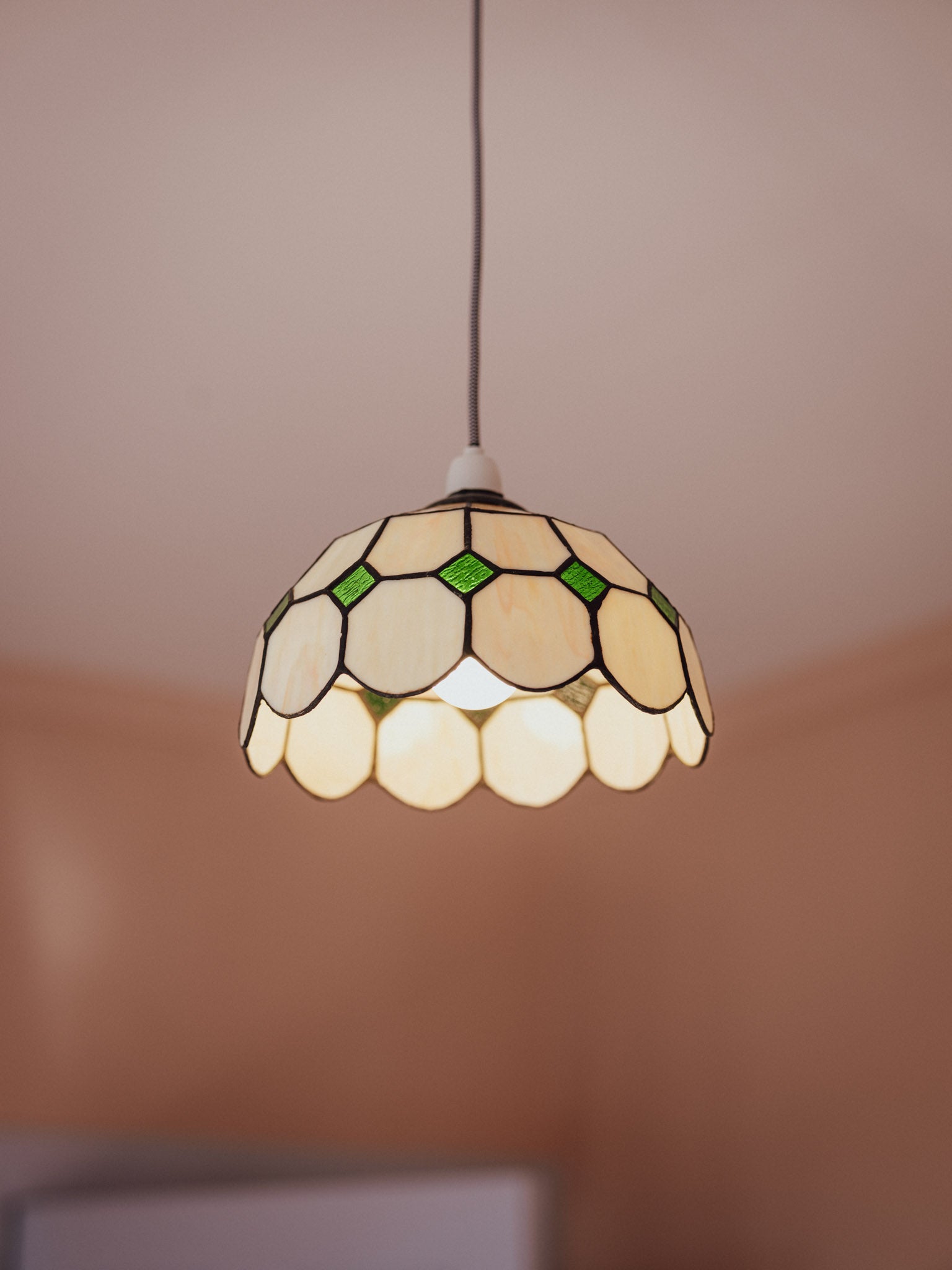 Stained glass pendant light with a white and green pattern on a neutral background