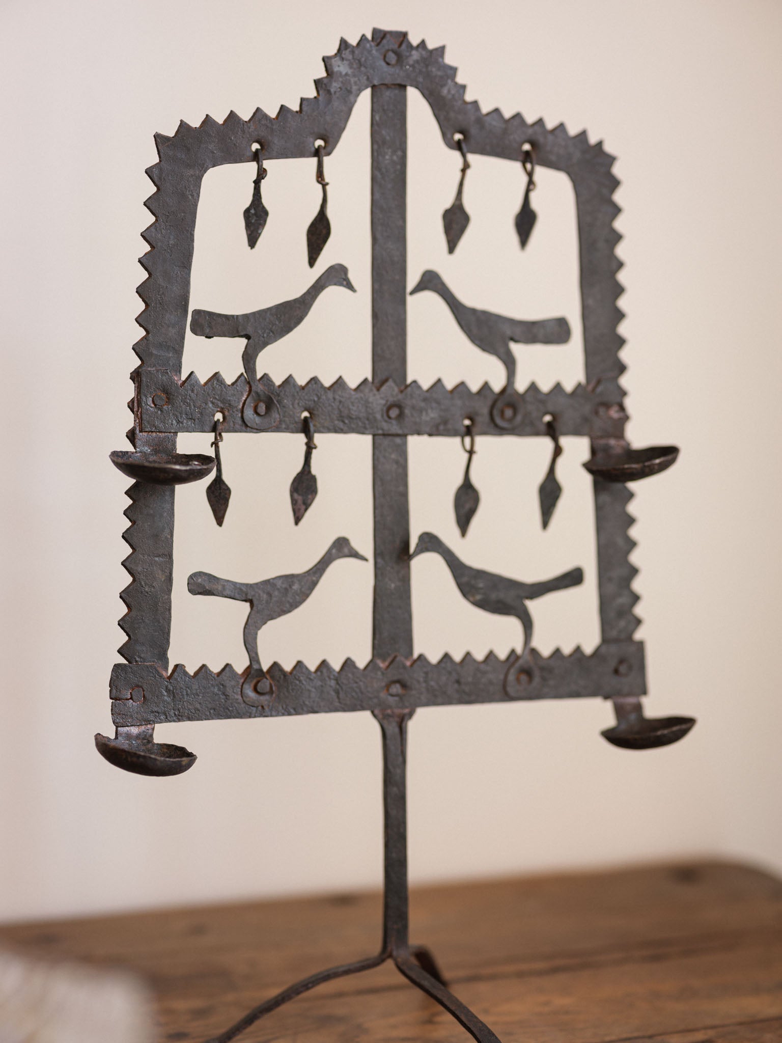 Decorative metal candle holder with bird designs on a wooden surface.