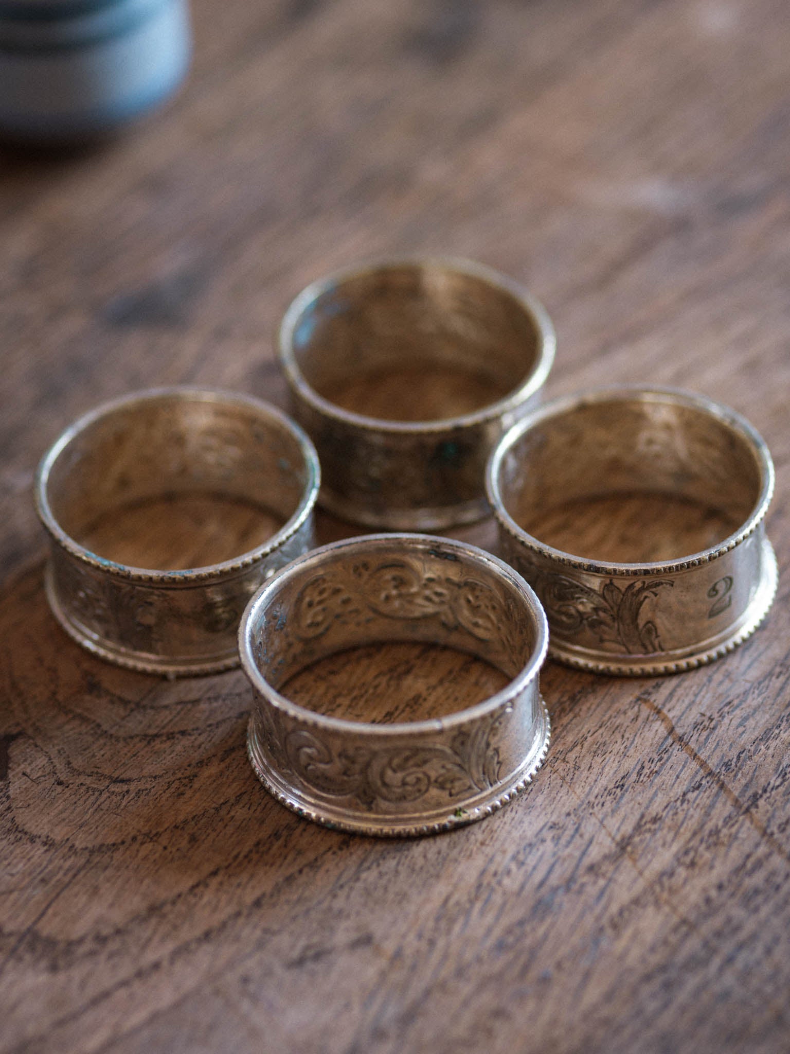 Four ornate silver napkin rings on a wooden surface