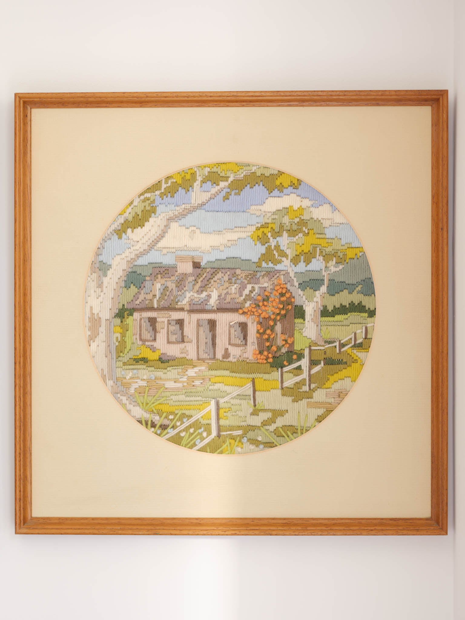 Framed artwork of a pastoral scene with a house and trees on a beige background