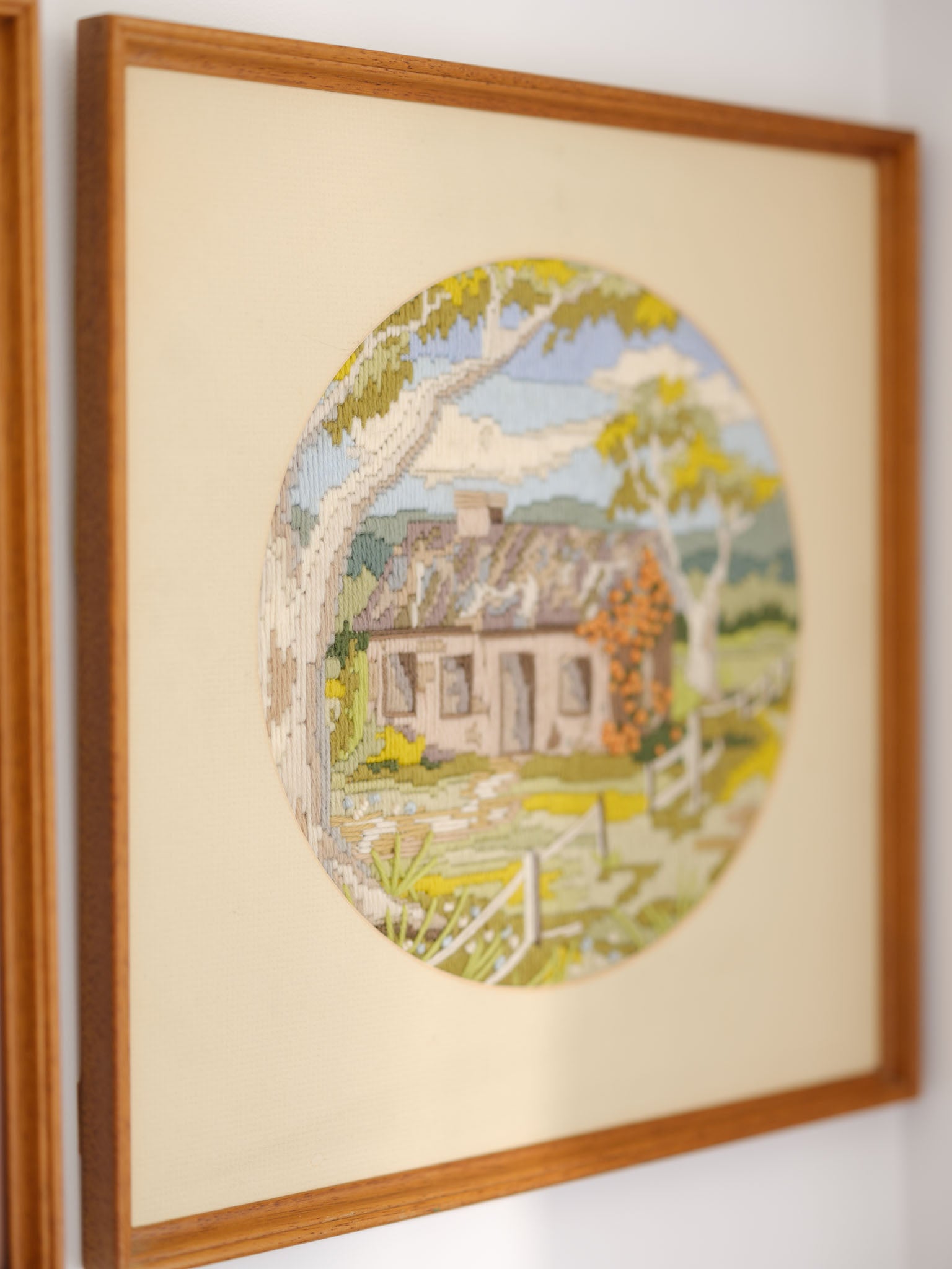 Framed embroidered picture of a house with trees on a beige background