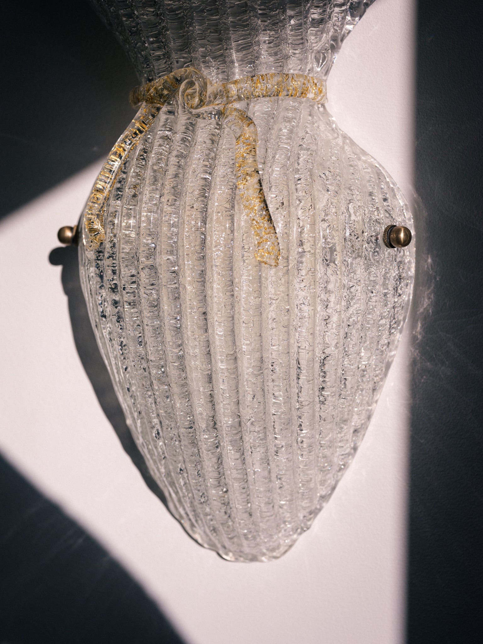 Vintage Murano glass wall sconce with ribbed clear glass and gold ribbon detailing. Italian mid-century wall light, hand-blown using the Graniglia technique. Mounted on a light grey backplate with brass fittings, perfect for hallways, bedrooms, or statement lighting.