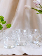 Set of clear glass tumblers with geometric patterns on a white surface with flowers and greenery.