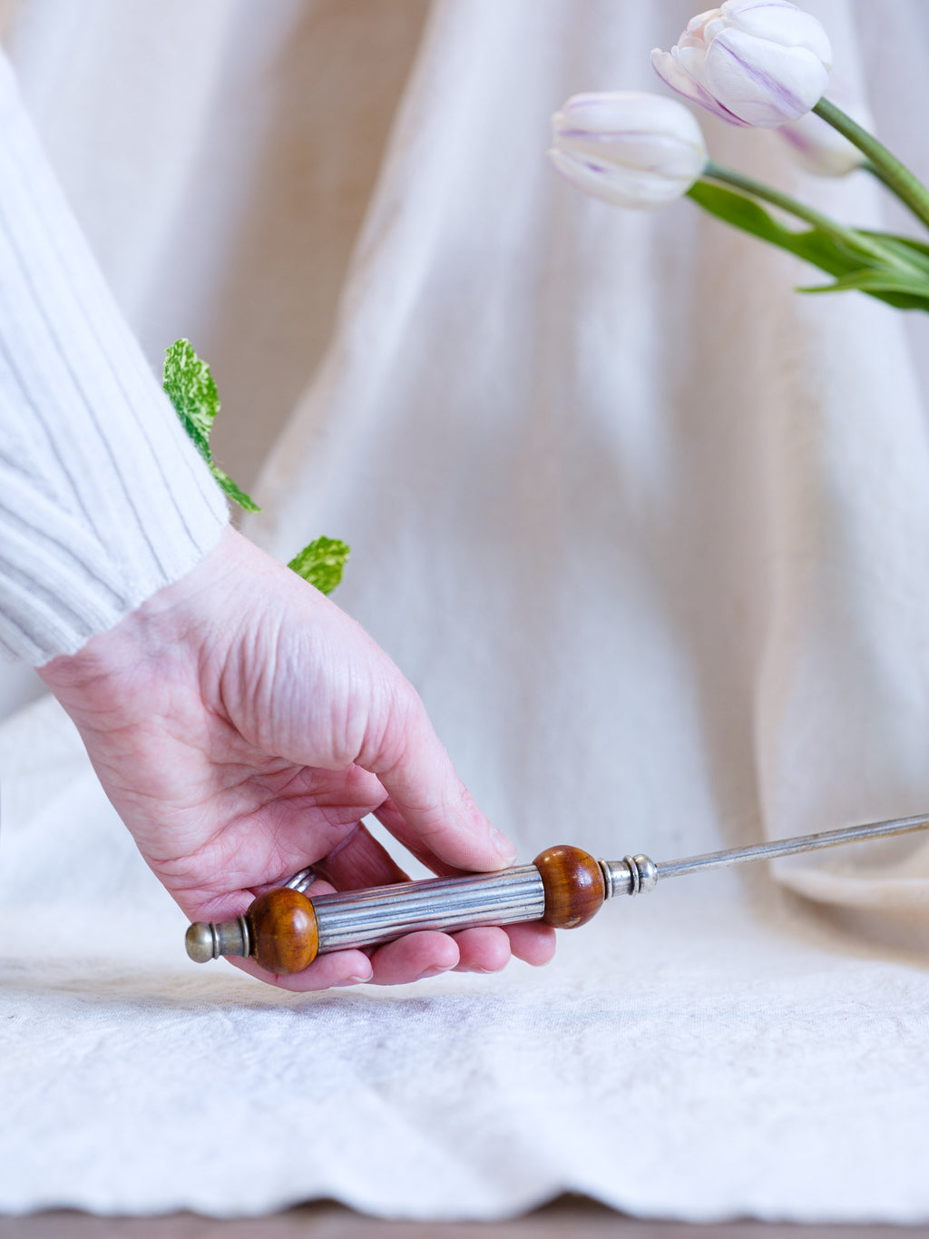Hand holding a wooden-handled tool with a blurred white background