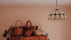 Decorative pendant light with stained glass shade hanging above wicker baskets on a beige wall.