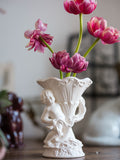 Decorative white vase with angel design holding pink flowers on a wooden surface.
