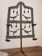 Decorative metal candle holder with bird designs on a wooden surface.