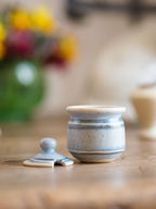 Small ceramic jar with lid on a wooden surface, blurred background