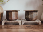 Two rustic metal pots on stone stands against a neutral background