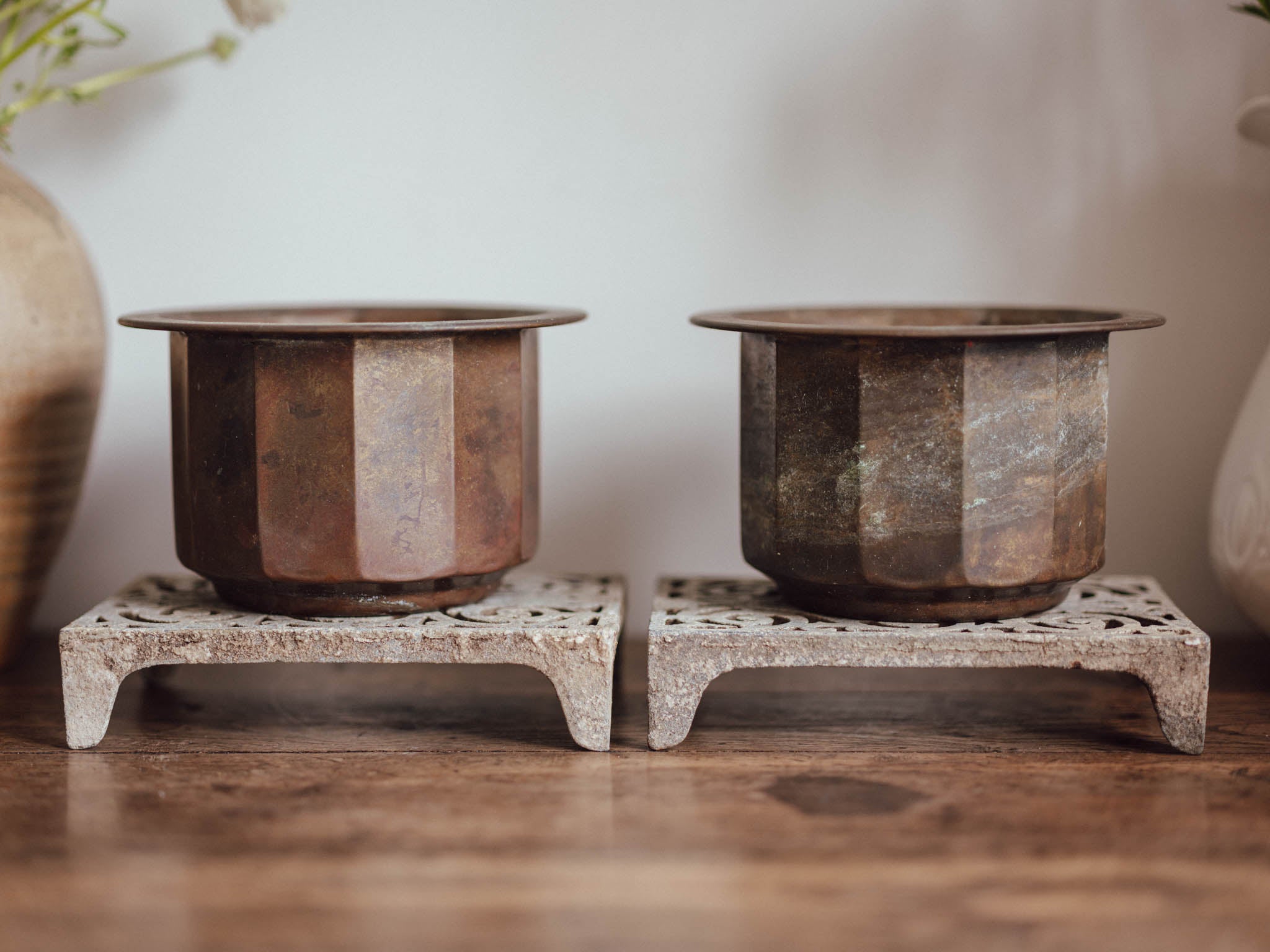 Two rustic metal pots on stone stands against a neutral background