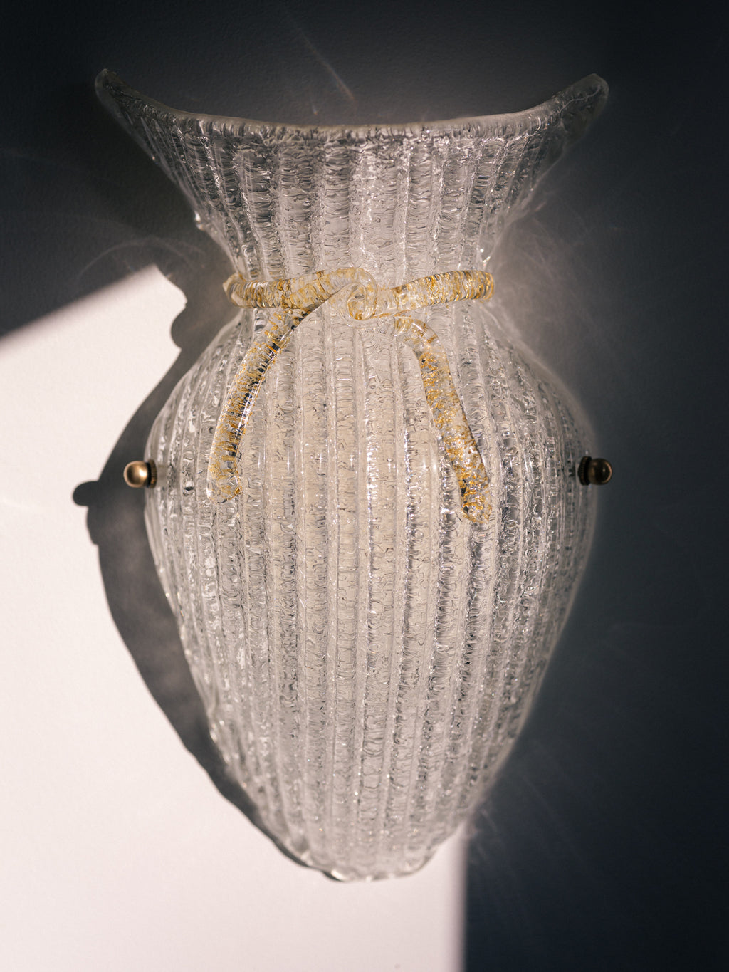 Vintage Murano glass wall sconce with ribbed clear glass and gold ribbon detailing. Italian mid-century wall light, hand-blown using the Graniglia technique. Mounted on a light grey backplate with brass fittings, perfect for hallways, bedrooms, or statement lighting.