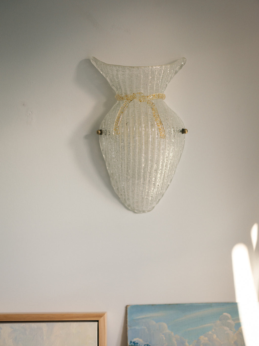 Vintage Murano glass wall sconce with ribbed clear glass and gold ribbon detailing. Italian mid-century wall light, hand-blown using the Graniglia technique. Mounted on a light grey backplate with brass fittings, perfect for hallways, bedrooms, or statement lighting.
