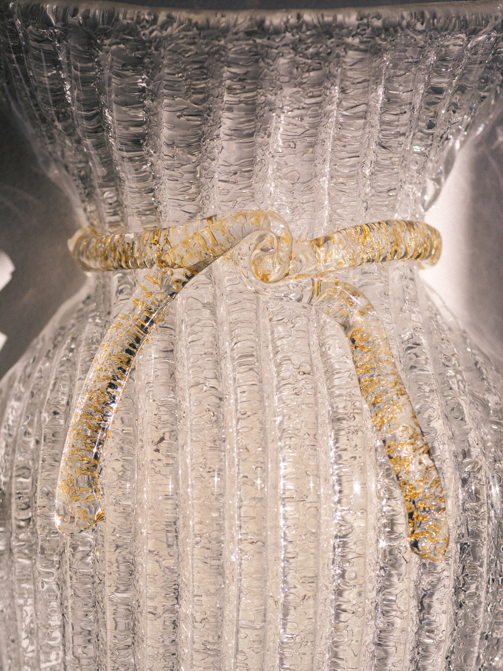 Vintage Murano glass wall sconce with ribbed clear glass and gold ribbon detailing. Italian mid-century wall light, hand-blown using the Graniglia technique. Mounted on a light grey backplate with brass fittings, perfect for hallways, bedrooms, or statement lighting.
