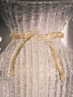 Vintage Murano glass wall sconce with ribbed clear glass and gold ribbon detailing. Italian mid-century wall light, hand-blown using the Graniglia technique. Mounted on a light grey backplate with brass fittings, perfect for hallways, bedrooms, or statement lighting.
