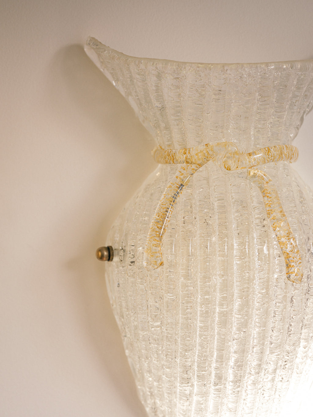 Vintage Murano glass wall sconce with ribbed clear glass and gold ribbon detailing. Italian mid-century wall light, hand-blown using the Graniglia technique. Mounted on a light grey backplate with brass fittings, perfect for hallways, bedrooms, or statement lighting.
