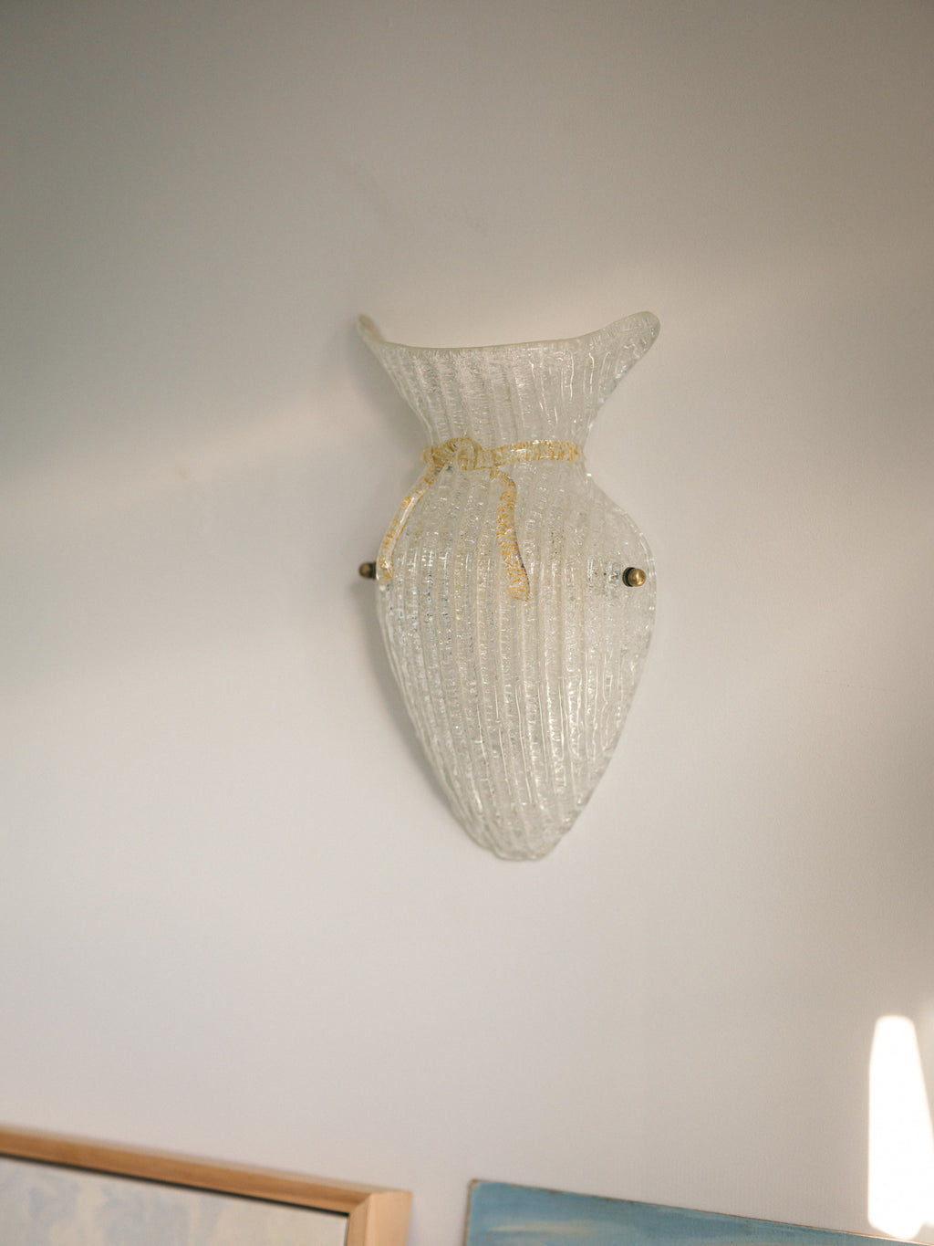 Vintage Murano glass wall sconce with ribbed clear glass and gold ribbon detailing. Italian mid-century wall light, hand-blown using the Graniglia technique. Mounted on a light grey backplate with brass fittings, perfect for hallways, bedrooms, or statement lighting.
